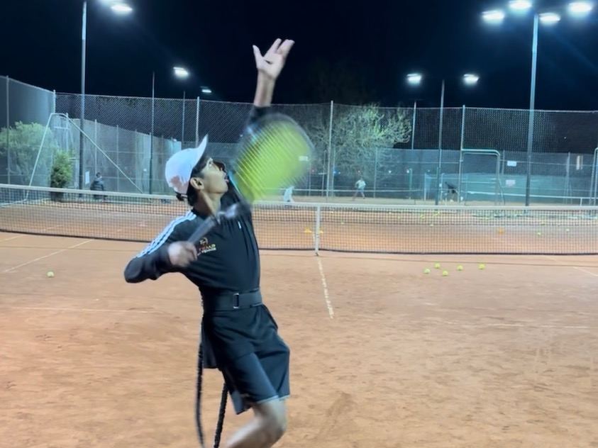 Junior player practising a forehand under lights during an evening class